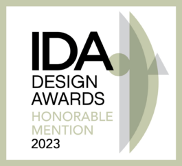 Logo of the IDA Design Awards 2023 featuring the text 'IDA Design Awards Honorable Mention 2023'. The text is placed on a white background with a light green border. A translucent abstract geometric shape overlaps the right side of the design. Filippos Fragkogiannis